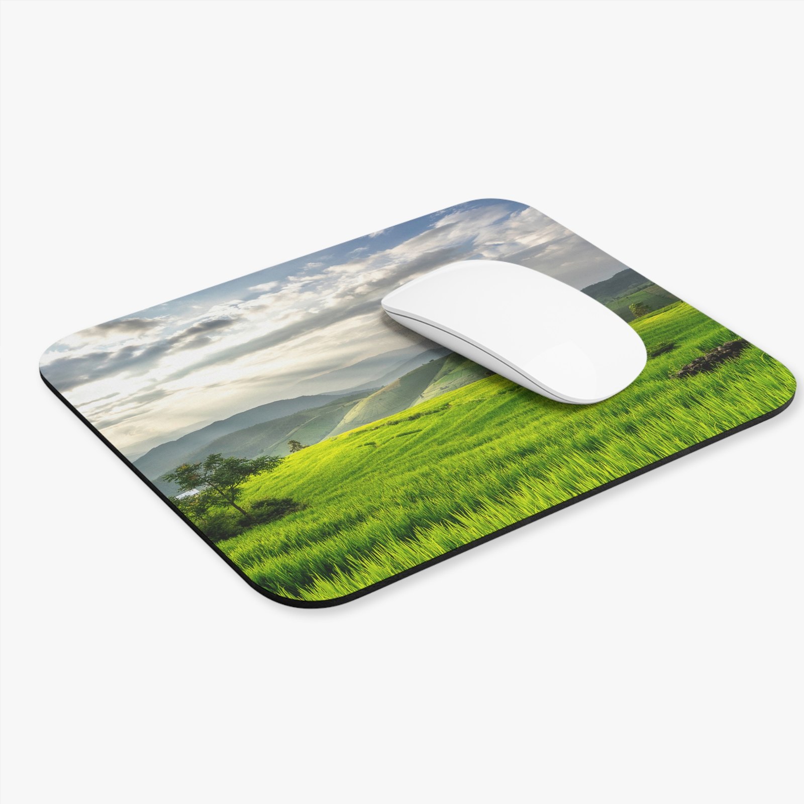Custom mouse pad printed with a green mountain landscape, on a desk with a white mouse on it